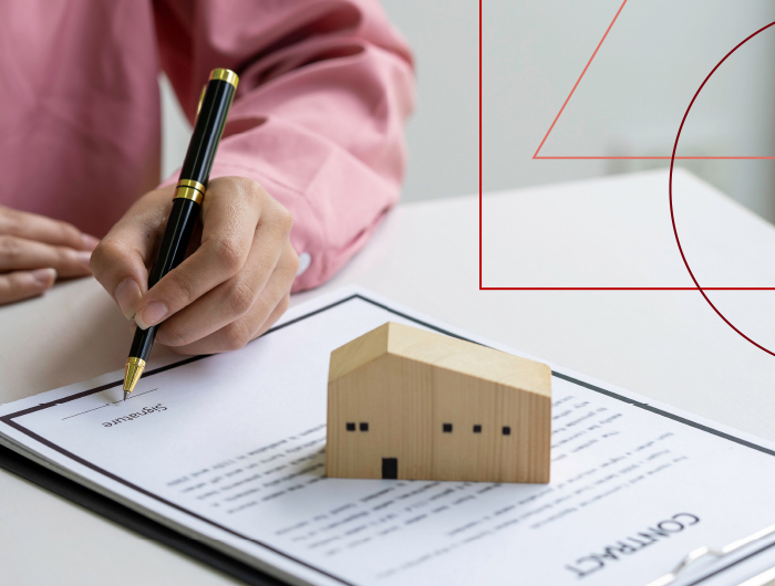 A person signing a contract next to a small model of a house, symbolizing a real estate transaction.