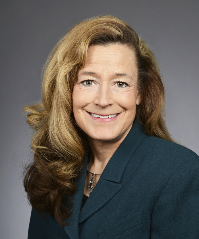 Woman in dark green suit, long hair, smiling at camera