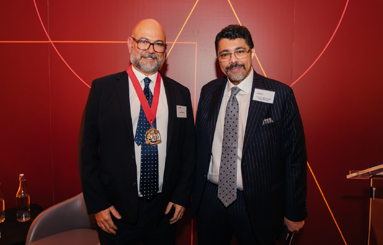 Two men in suits, smiling, against a red background