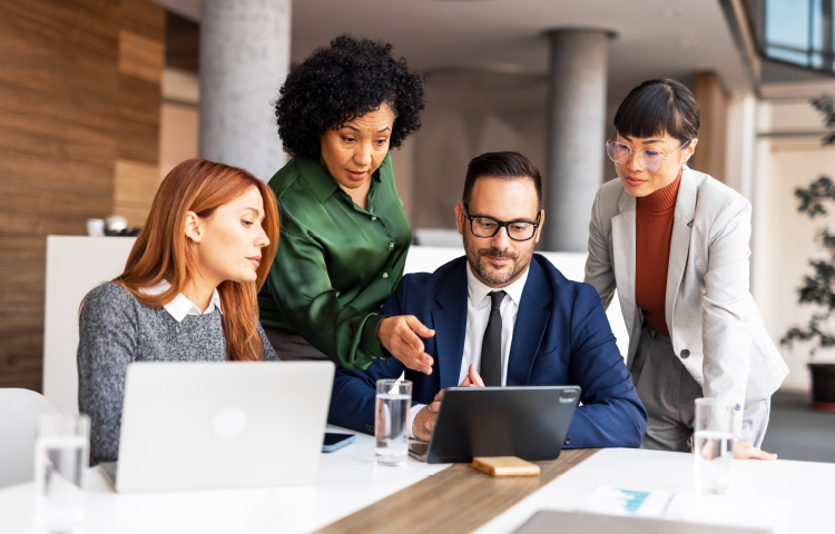 Four people talking and looking at a laptop screen in an office